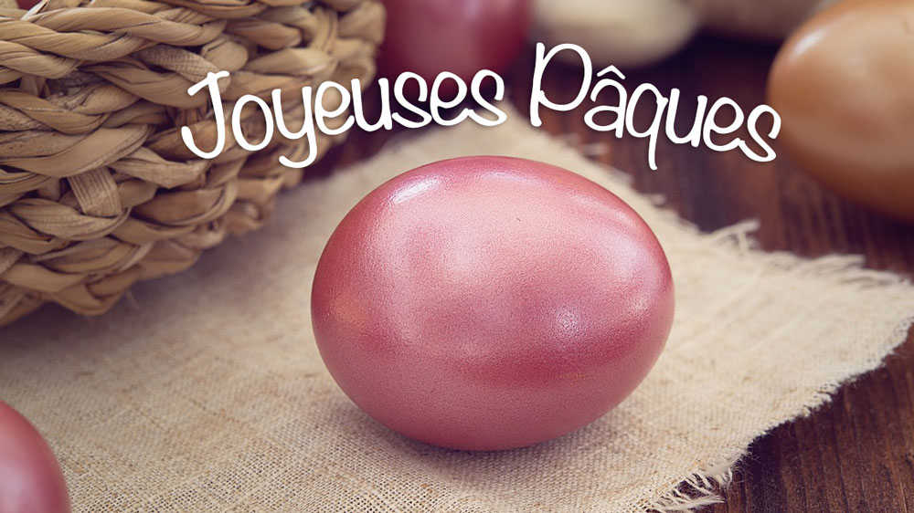 Image de voeux de Pâques avec un œuf en chocolat rose et une phrase de bons voeux. En arrière-plan, il y a un panier de Pâques avec d'autres cadeaux.